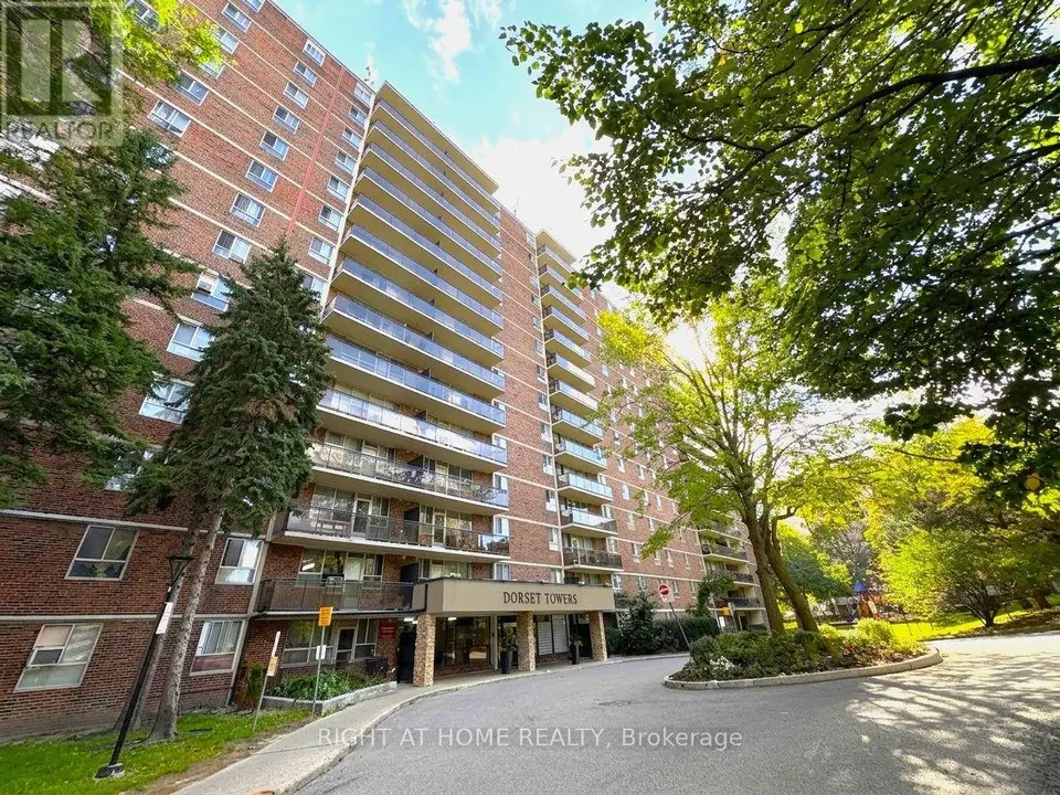 Low-angle view of a brick high-rise with balconies, a Dorset Towers entrance canopy, circular driveway and mature trees.