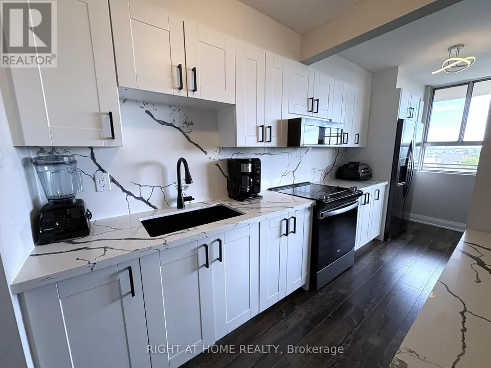 Kitchen counter with black undermount sink and faucet, veined quartz backsplash, black range, microwave, refrigerator and window at far end.