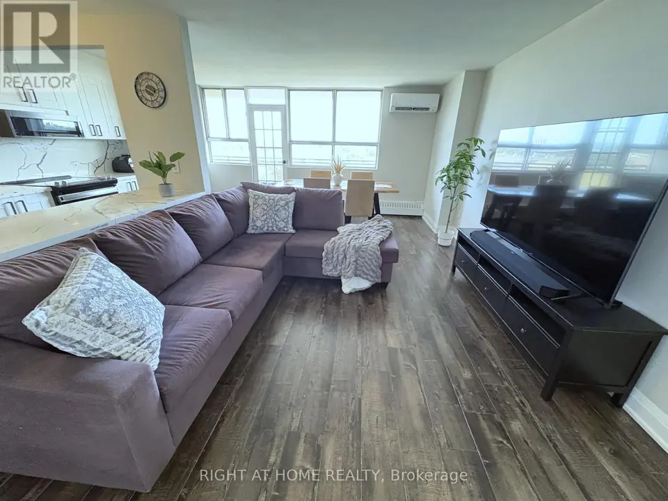 Purple sectional and TV console in living room, kitchen counter at left, dining table and windows in background.